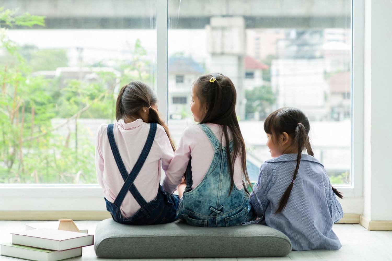 Three young children sitting by a window with books, reading together