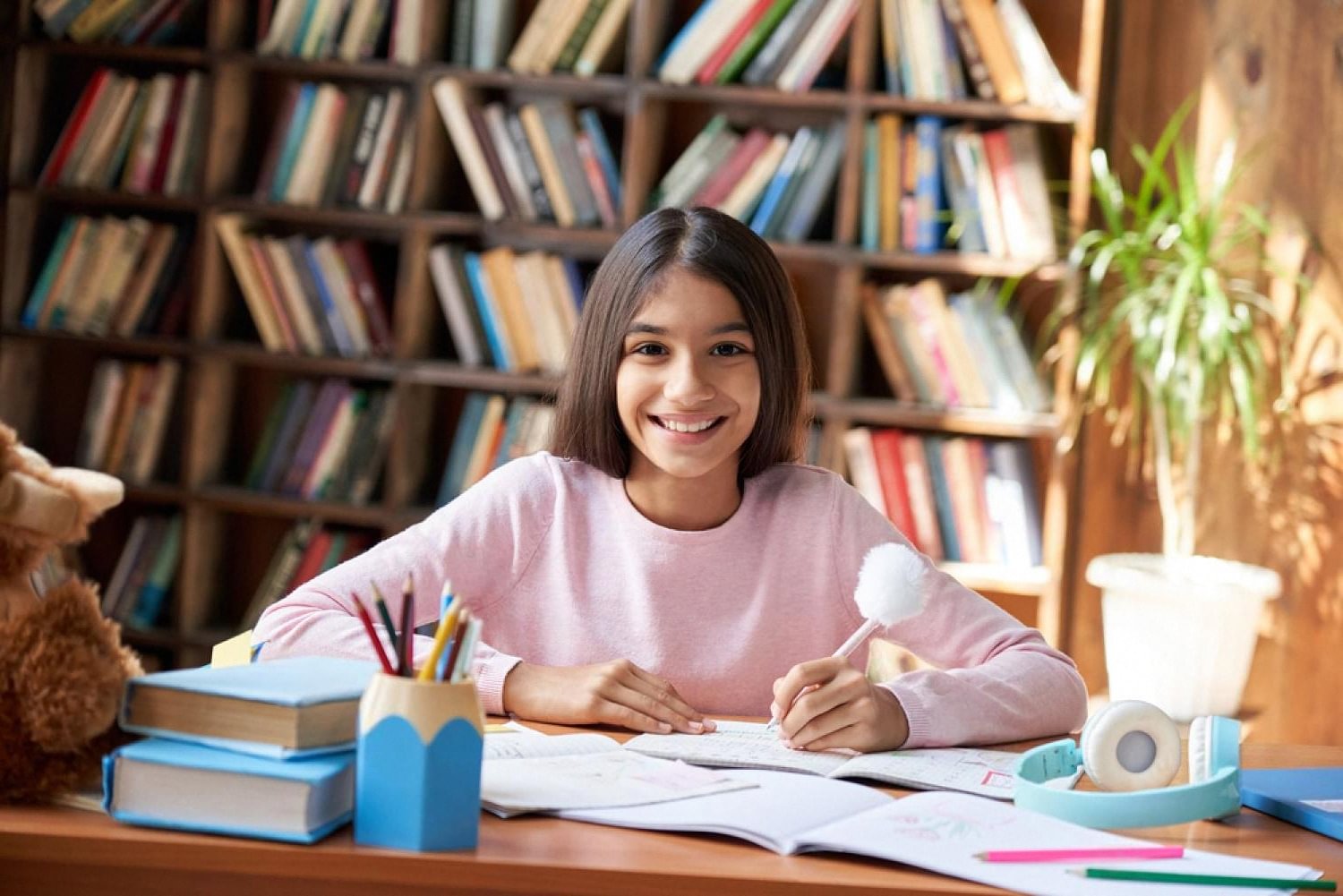 Girl in a school library smiling at her desk with books and pencils